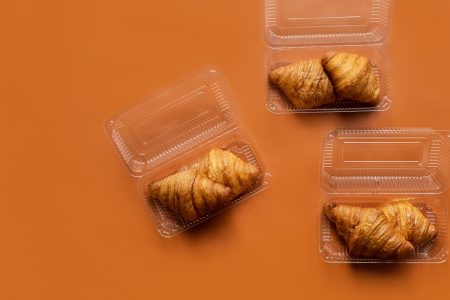 Freshly baked croissants in plastic packaging on an orange background. Takeaway food concept. French and American Croissants are enjoyed worldwide.Croissants background: top view, flat lay